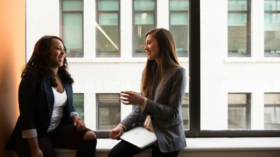 Two woman sitting in front of a window, chatting.