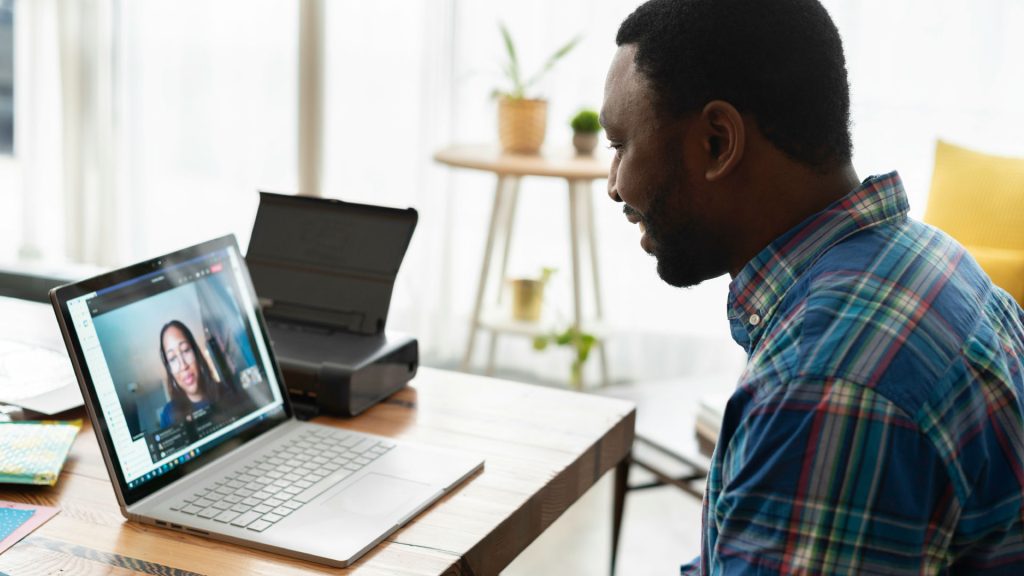 A man sitting at a table video chats with a woman on the laptop screen in front of him.