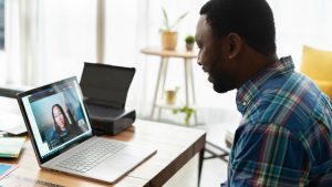 A man sitting at a table video chats with a woman on the laptop screen in front of him.